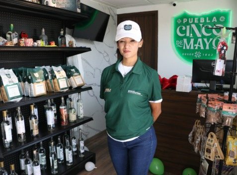 Punto de venta poblano con productos artesanales y licores que portan el distintivo Marca Puebla Cinco de Mayo, atendido por una colaboradora